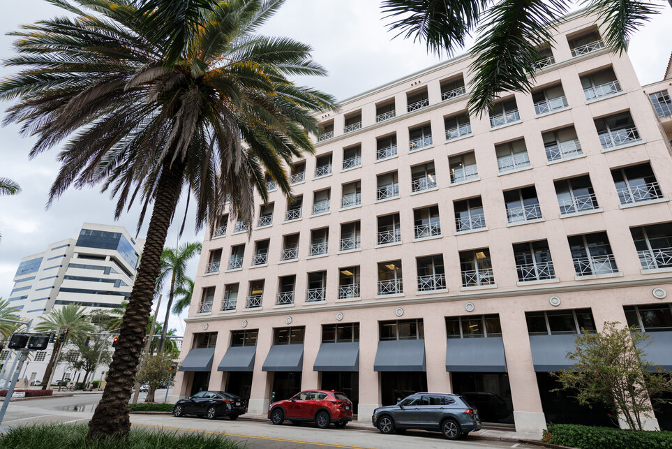 Ein weißes, siebenstöckiges Gebäude mit rotem Dach blickt auf einen großen, rosa gefliesten Innenhof mit einem zentralen Teich, grünen Sträuchern und Sitzgelegenheiten auf dem Kellogg-Miami-Campus