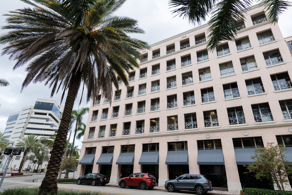 A white seven-storey building with a red roof overlooks a large pink-tiled courtyard with a central pond, green shrubs and seating areas on Kellogg-Miami campus