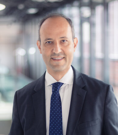 A man in a suit and blue tie looks into the camera