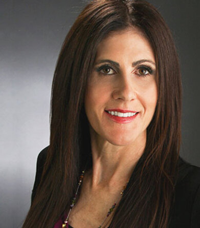 A woman with dark hair in an black blazer looks into the camera