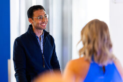 A smiling man in a blue shirt engaged in conversation with a woman