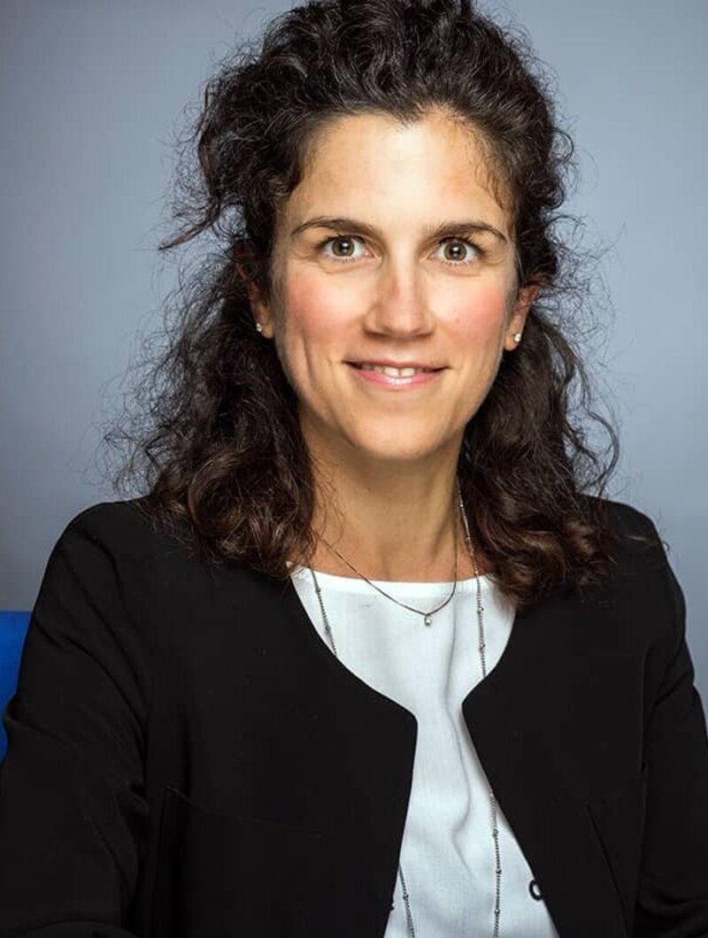 A woman in a dark suit looks friendly into the camera