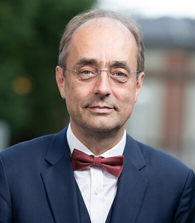 An older gentleman in a suit and bow tie looks into the camera