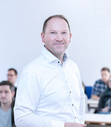 A man in a white shirt stands in front of a group in a lecture hall