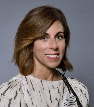 A woman in a light blouse and dark hair looks friendly into the camera