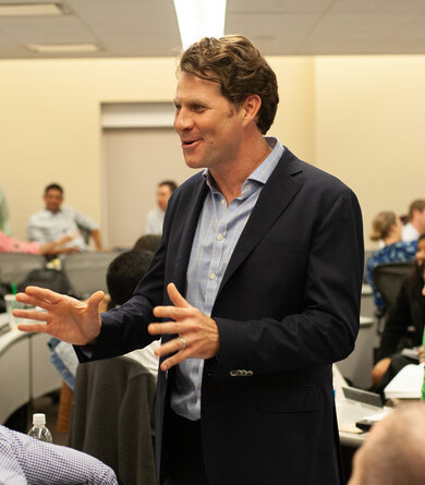 A man stands in the middle of a group and speaks with enthusiastic facial expressions and gestures